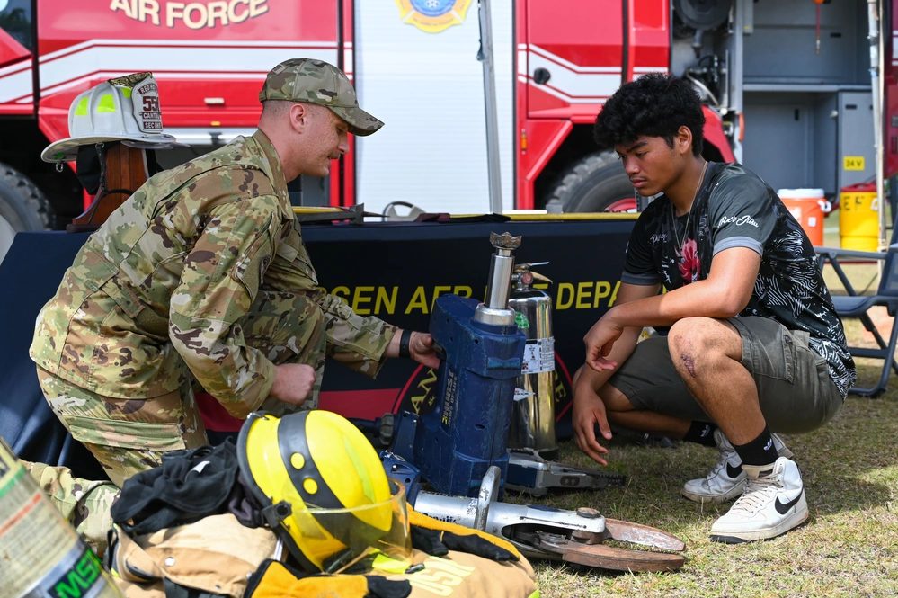 A firefighter shows a high school student how hydraulic rescue tools work beside a fire engine