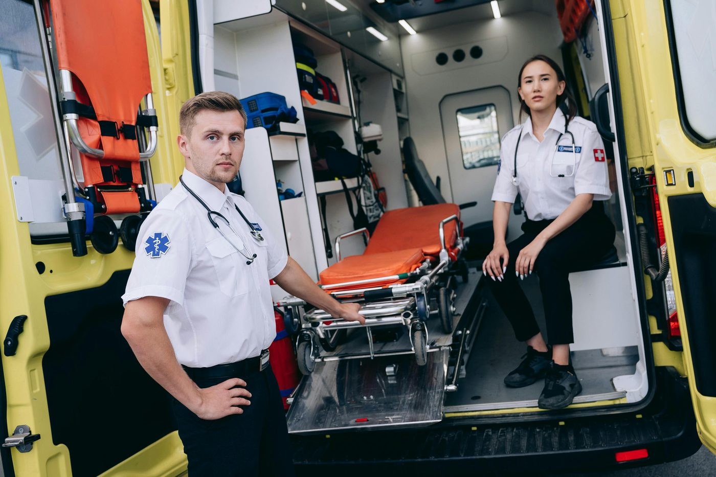 Two EMTs standing at the open rear doors of an ambulance with the stretcher loaded