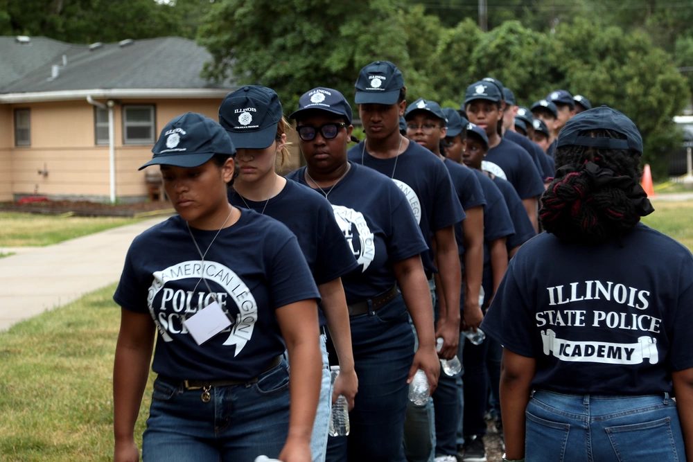 A column of police cadets in matching academy shirts and caps marching in formation